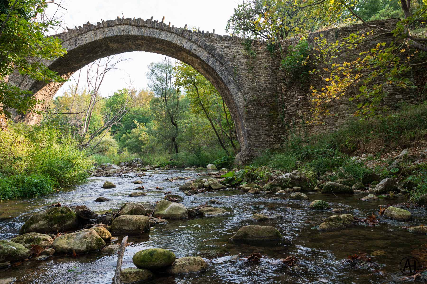 An arched stone bridge over a rocky stream