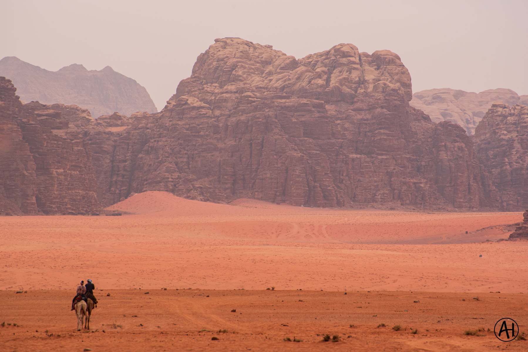 A rider crossing red desert sand beneath towering cliffs
